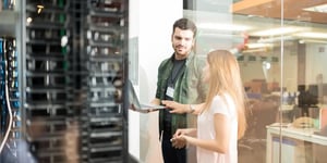 Two business people standing in server room with laptop and discussing